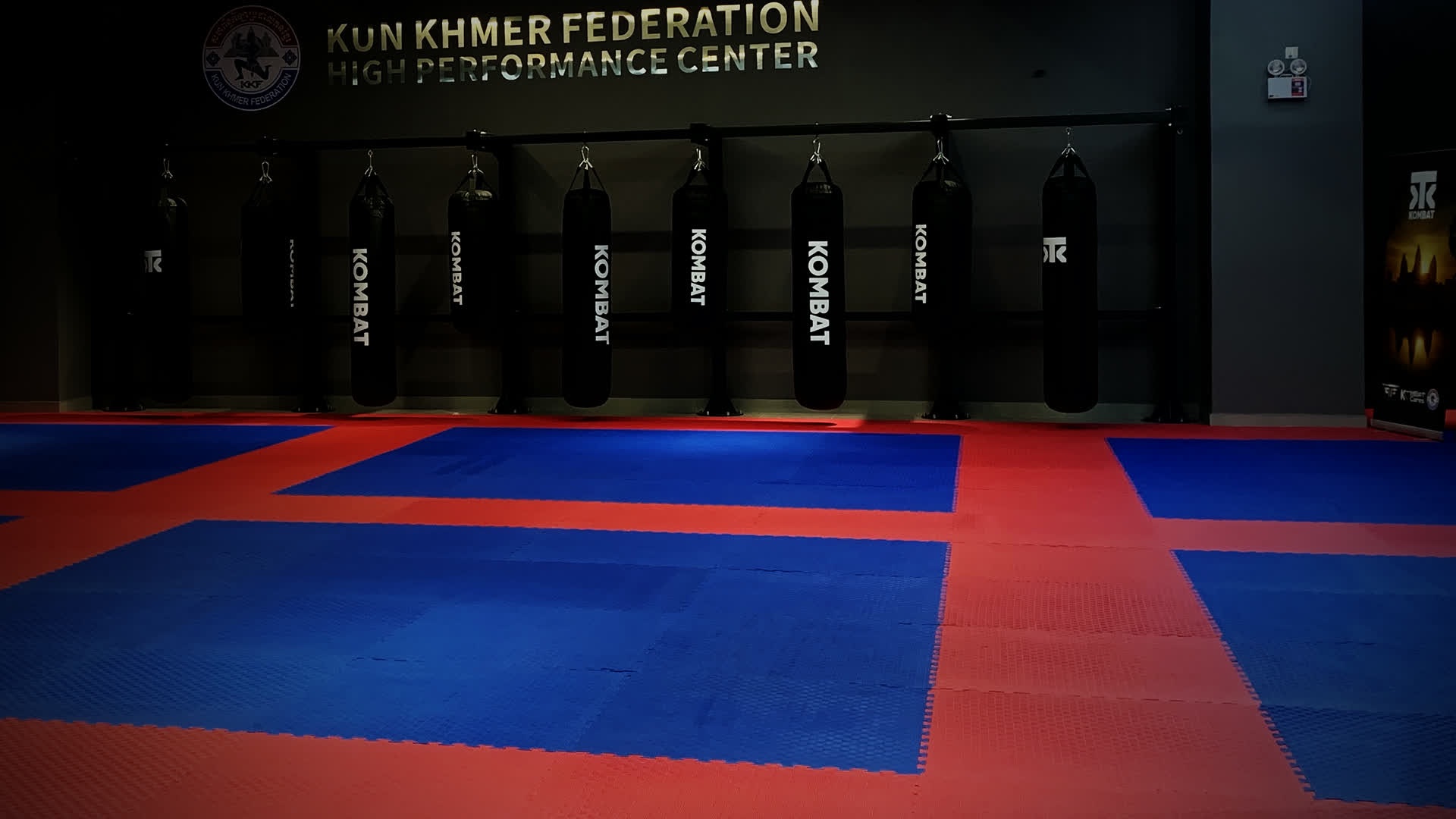 The bag wall and mats at Kombat Academy under the Kun Khmer Federation High Performance Center sign